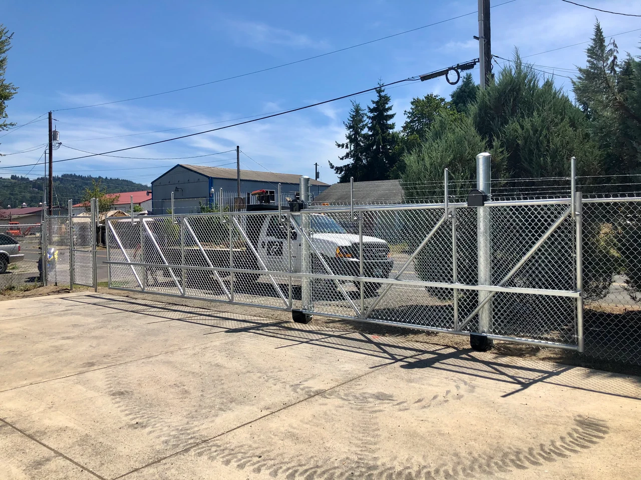 A wide chain link sliding gate with support rollers and diagonal bracing closes a paved commercial entrance.